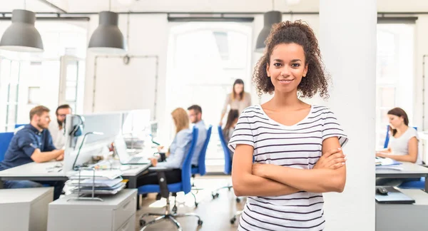 Portrait of young confident woman leader standing in office with team on background