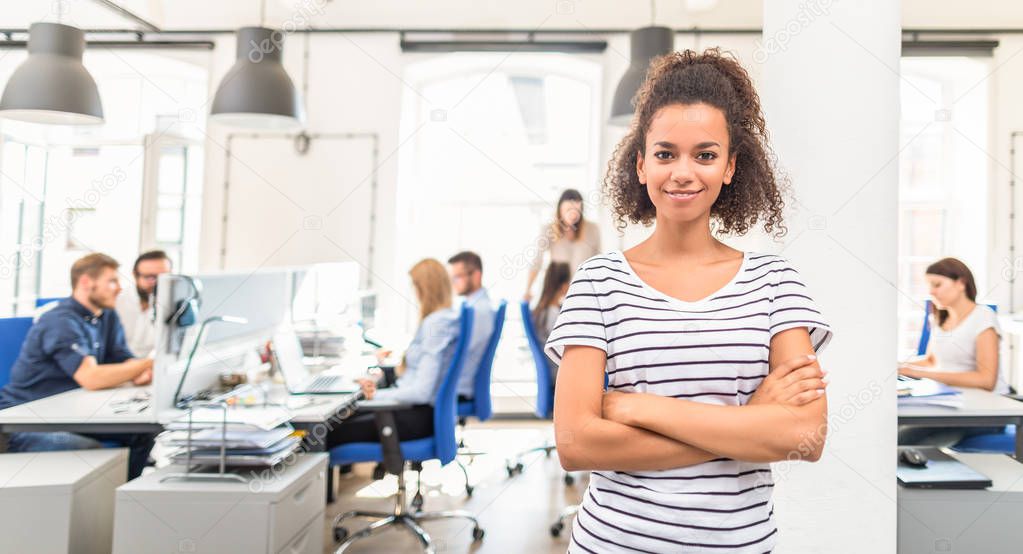 Portrait of young confident woman leader standing in office with team on background