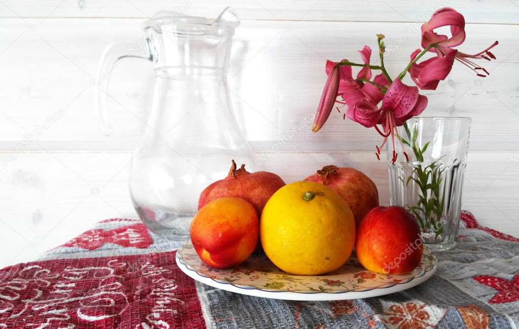  fruits lie on a plate, a glass carafe and a glass with a flower