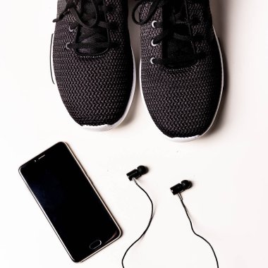flatlayconcept: çift siyah spor ayakkabı, siyah mobilephone ve l Siyah kulaklık. Beyaz Bankamatik her şeyde
