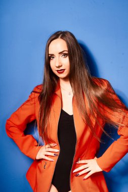  Siyah vücut ve turuncu ceket giyen, mavi arka planda, zıt görüşlü genç bir kız.          