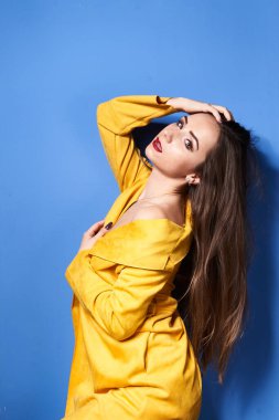  Güzel bir kız mavi bir duvara karşı sarı bir ceketle poz veriyor.           