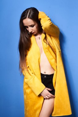  Güzel bir kız mavi bir duvara karşı sarı bir ceketle poz veriyor.           