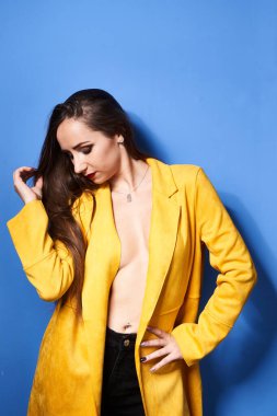  Güzel bir kız mavi bir duvara karşı sarı bir ceketle poz veriyor.                 