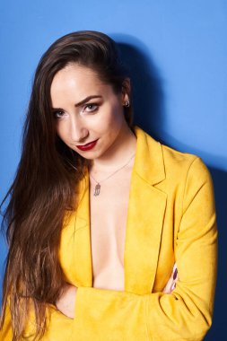  Güzel bir kız mavi bir duvara karşı sarı bir ceketle poz veriyor.                 