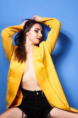  Güzel bir kız mavi bir duvara karşı sarı bir ceketle poz veriyor.                 