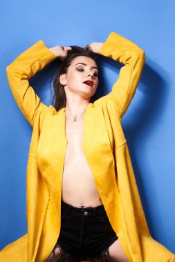  Güzel bir kız mavi bir duvara karşı sarı bir ceketle poz veriyor.                 