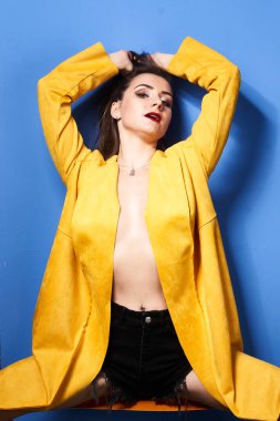  Güzel bir kız mavi bir duvara karşı sarı bir ceketle poz veriyor.           