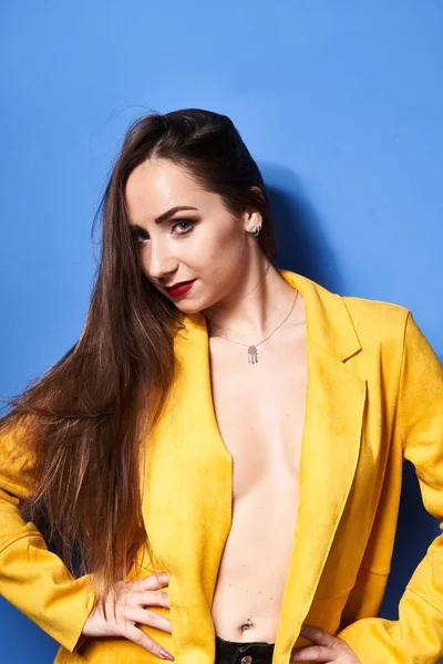  Güzel bir kız mavi bir duvara karşı sarı bir ceketle poz veriyor.           