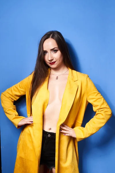 一个漂亮的姑娘穿着一件黄色的外套靠着蓝色的墙摆姿势 — 图库照片