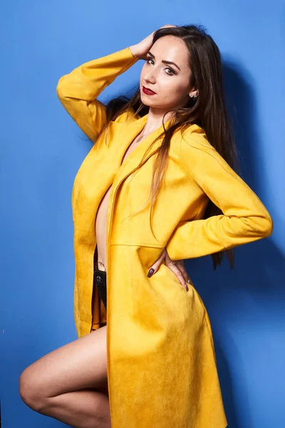  Güzel bir kız mavi bir duvara karşı sarı bir ceketle poz veriyor.           