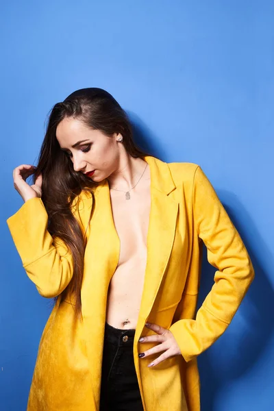 一个漂亮的姑娘穿着一件黄色的外套靠着蓝色的墙摆姿势 — 图库照片