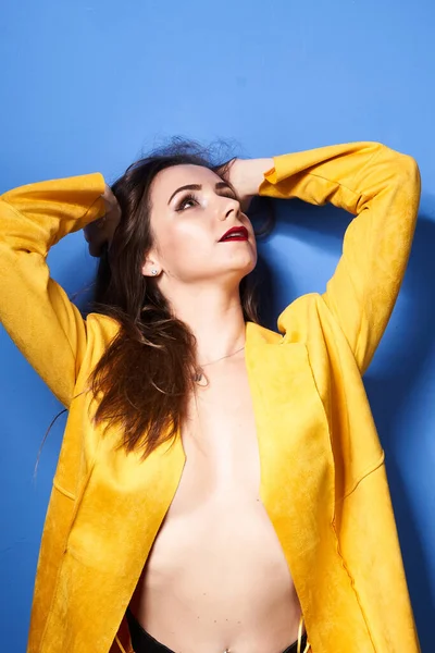  Güzel bir kız mavi bir duvara karşı sarı bir ceketle poz veriyor.                 
