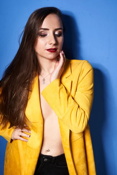  Güzel bir kız mavi bir duvara karşı sarı bir ceketle poz veriyor.                 