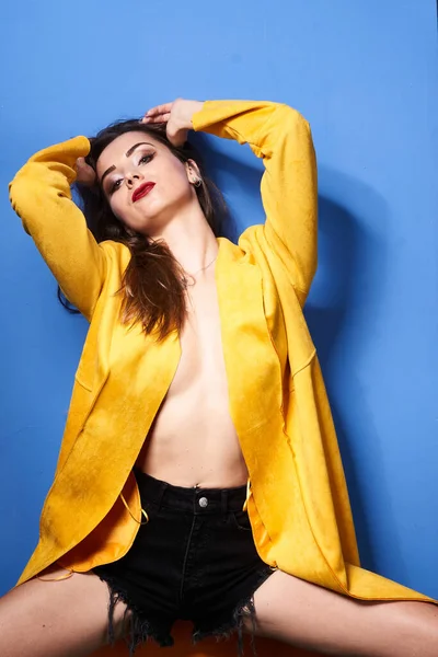  Güzel bir kız mavi bir duvara karşı sarı bir ceketle poz veriyor.                 