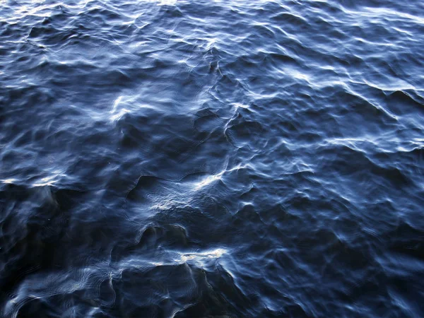 Blue water surface, light waves with sun flares, may be used as background or texture