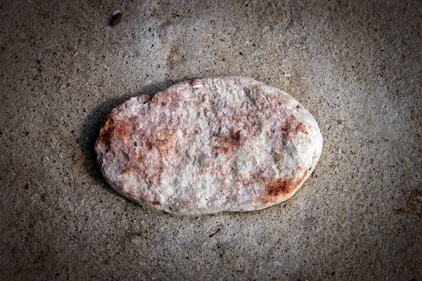 Small flat pink granite stone with red inclusions half fixed in concrete surface, background with darkened vignette