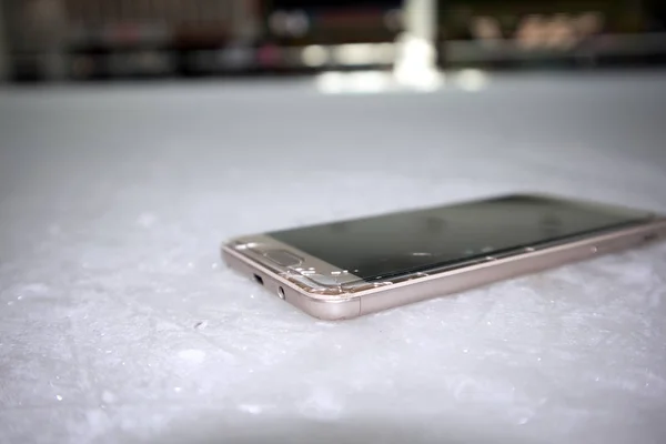 Modern smart phone with cracked screen glass lying on scratched ice