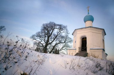 Çıplak ağaca yakınlarındaki snowed bir tepe üzerinde beyaz taştan küçük Ortodoks Kilisesi