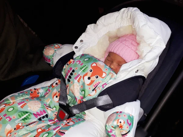 Swaddled newborn girl sleeping in the car strapped in booster seat