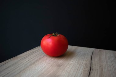Ahşap bir tahtada duran tek olgun kırmızı domates, siyah arka planda.