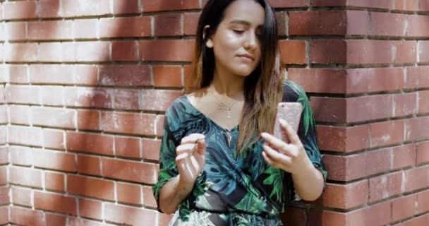 Женщина опирается на кирпичную стену с помощью мобильного телефона — стоковое видео