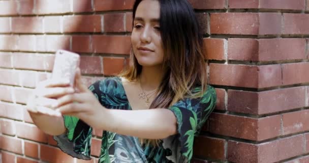 Mujer tomando una selfie delante de una pared de ladrillo — Vídeo de stock