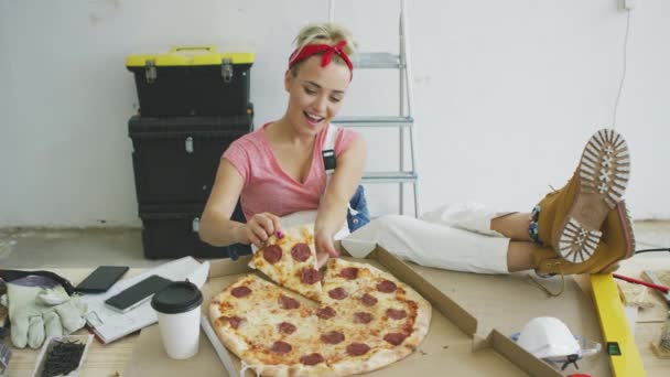 Mujer en overol comiendo pizza en el lugar de trabajo — Vídeo de stock