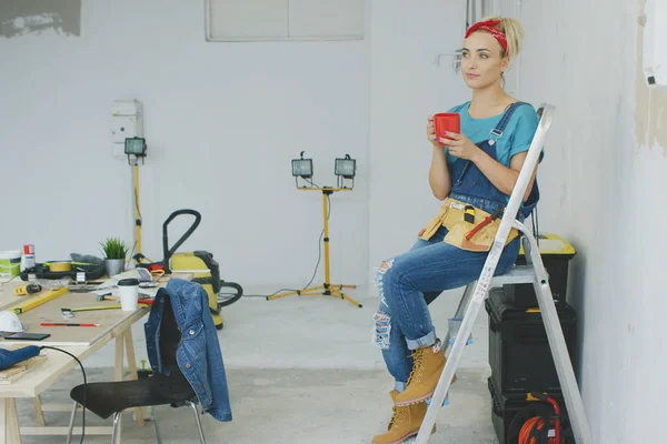 Female carpenter resting on stepladder with beverage — Stock Photo, Image