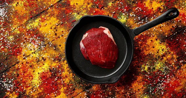 Carne en la sartén colocada en la superficie con especias derramadas — Foto de Stock