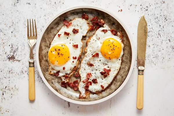 Twee verse gebakken eieren met knapperig knapperig spek geserveerd op rustieke bord — Stockfoto