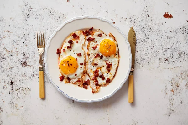 Dvě čerstvé smažené vejce s křupavé křupavé slaniny a pažitkou podávaná na rustikální talíř — Stock fotografie
