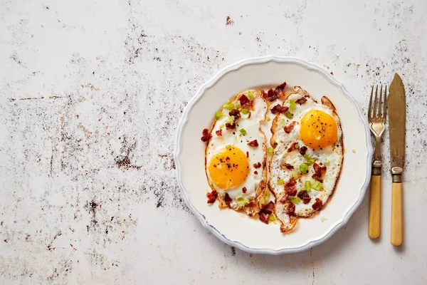 Dois ovos fritos frescos com bacon crocante crocante e cebolinha servida em prato rústico — Fotografia de Stock