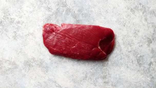 Шматок сирого свіжого яловичого стейка, розміщеного на сірому кам'яному фоні — стокове відео