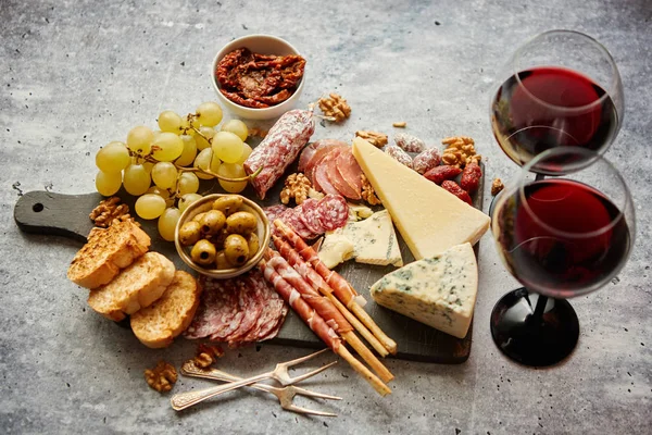 Tablero de aperitivos fríos con carnes, uvas, vino, varios tipos de queso —  Fotos de Stock