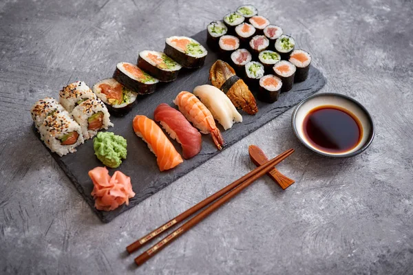 Composición de diferentes tipos de rollos de sushi colocados en tablero de piedra negro — Foto de Stock