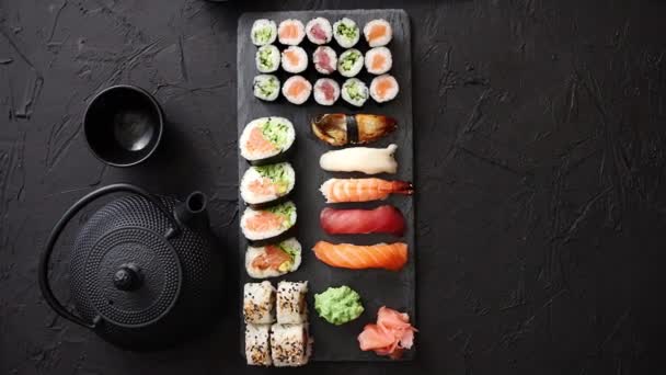 Ποικιλία από διαφορετικά είδη sushi ρολά τοποθετημένα στο μαύρο του σκάφους πέτρα — Αρχείο Βίντεο