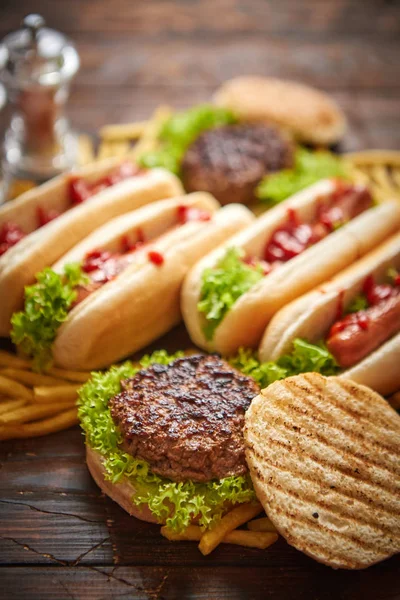 Um sortimento de comida rápida. Hambúrgueres e cachorros-quentes colocados na mesa de madeira enferrujada — Fotografia de Stock