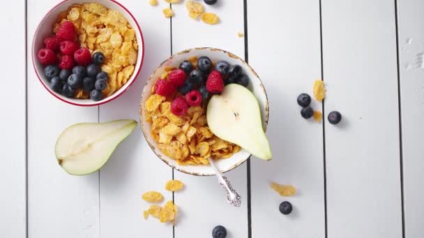 Golden cornflakes with fresh fruits of raspberries, blueberries and pear in ceramic bowl — Stock Video