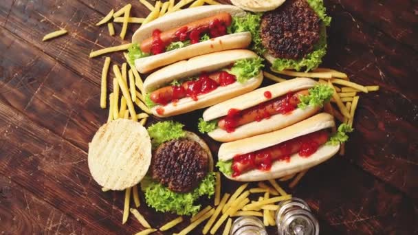 Asortyment fast foodów. Hamburgery i hot dogi umieszczone na zardzewiałym drewnianym stole — Wideo stockowe