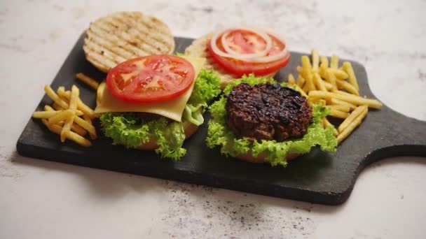 Два вкусных гамбургера домашнего приготовления с говядиной, помидорами, луком и салатом — стоковое видео