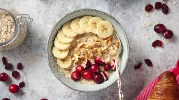 Ceramic bowl of oatmeal porridge with banana, fresh cranberries and walnuts — Stock Video