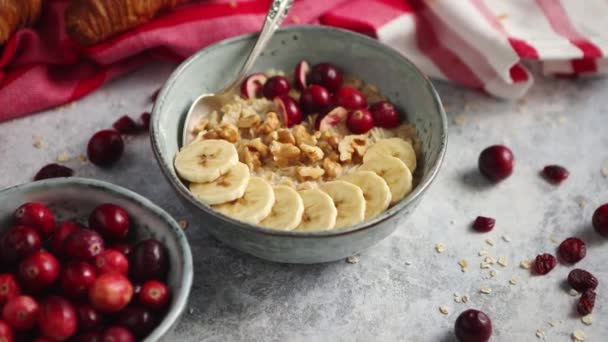 Keramikskål med havregrynsgröt med banan, färska tranbär och valnötter — Stockvideo