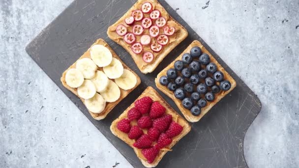 Rebanadas de pan integral con mantequilla de maní y varias frutas — Vídeo de stock