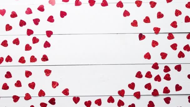 Состав ко Дню святого Валентина. Блёстки в форме сердца на белом деревянном столе — стоковое видео