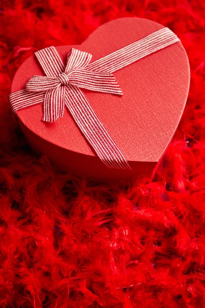 Cadeau en forme de coeur, placé sur fond de plumes rouges — Photo