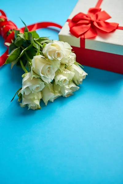 白色玫瑰的花束与红色弓在蓝色背景。侧面的盒装礼物 — 图库照片