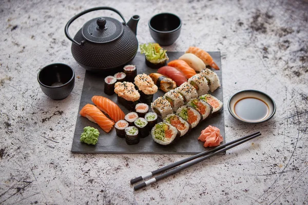 Assortment of different kinds of sushi rolls placed on black stone board — Stock Photo, Image