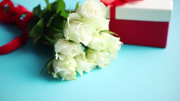 白色玫瑰的花束与红色弓在蓝色背景。侧面的盒装礼物 — 图库视频影像