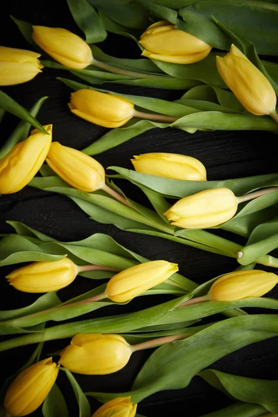 Жовті тюльпани розміщені на чорному столі. Вид зверху з плоским ліжком — стокове фото